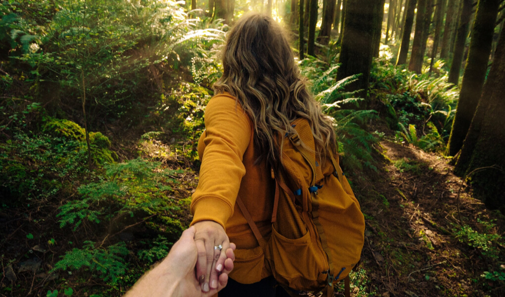 Photo of a woman holding somebody's hand on a walk through a forest
