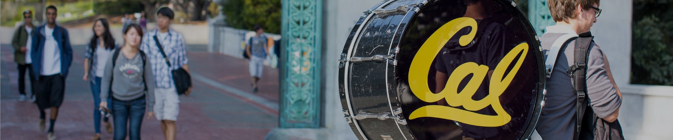 Photo of a Cal marching band member carrying a bass drum near Sather Gate