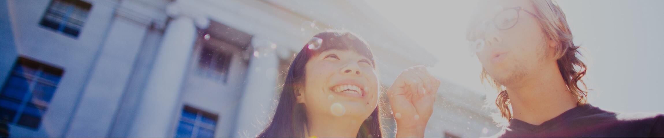 A girl and a guy with the sun behind them, guy blowing bubbles and girls smiling