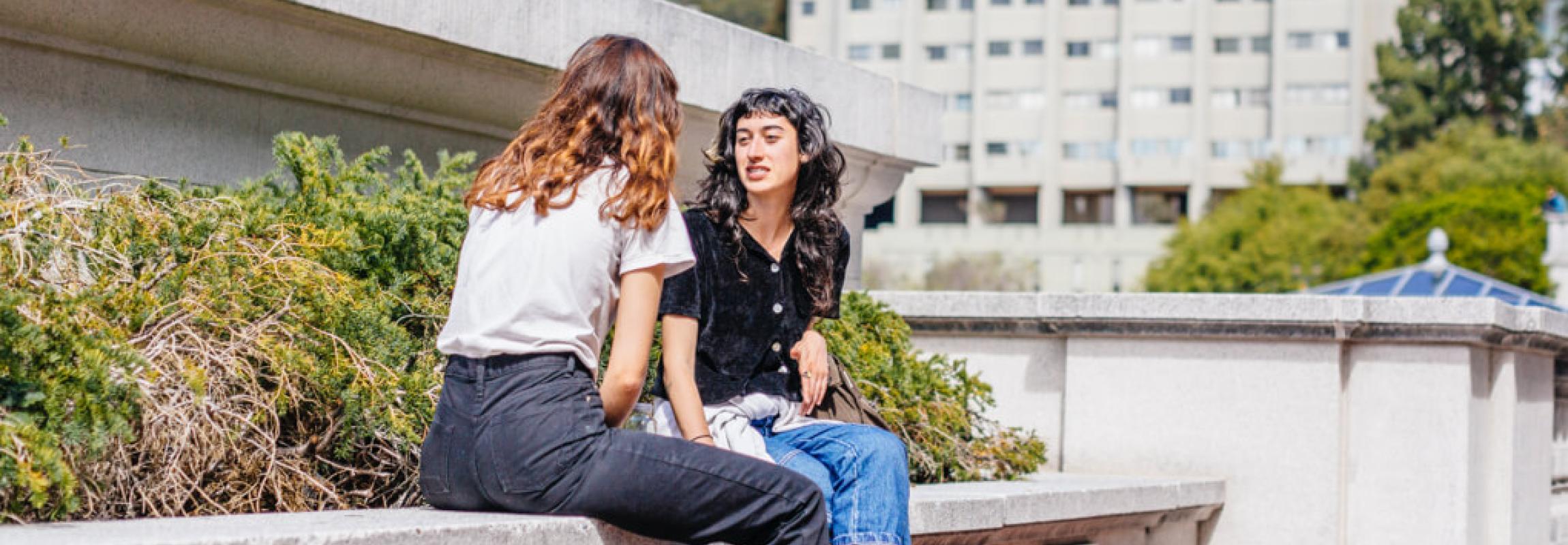 Photo of two female students sitting outside having a conversation